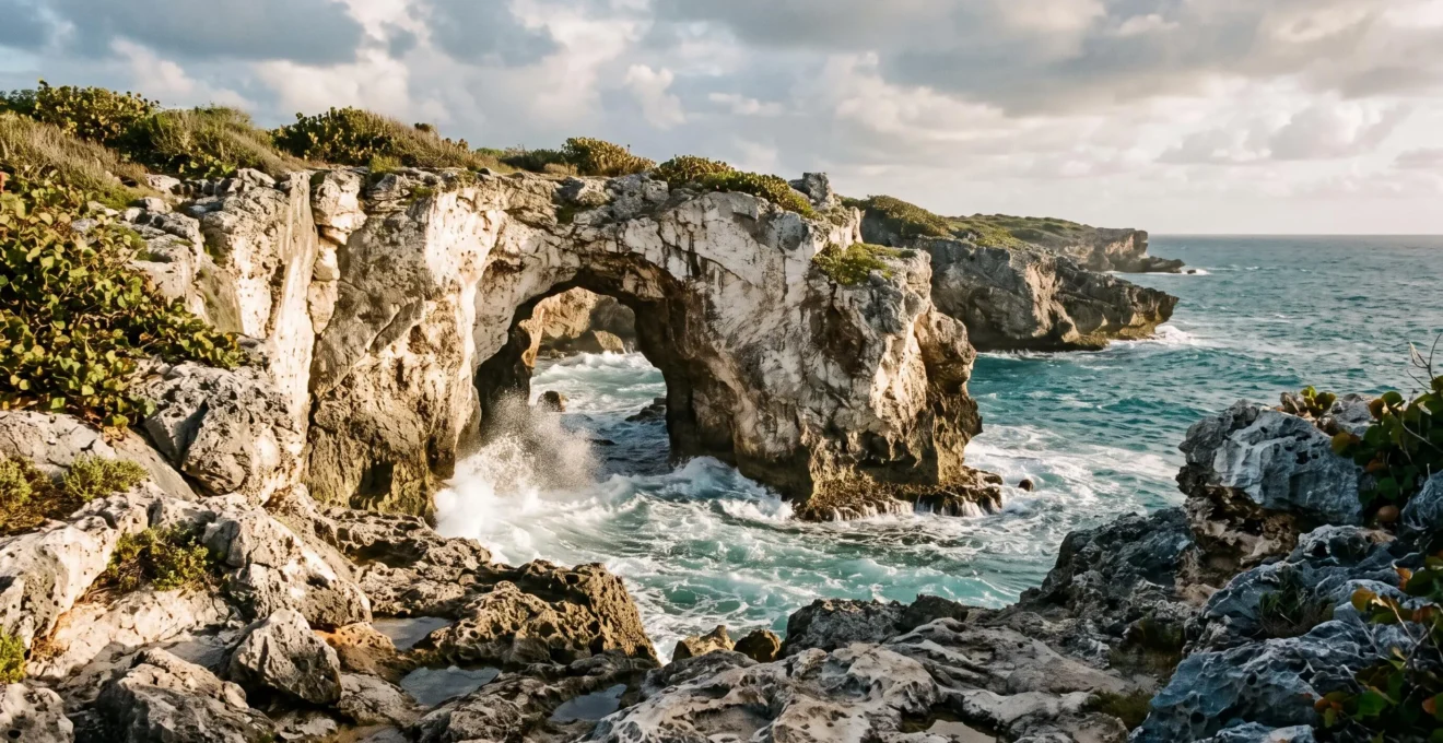 Arche rocheuse naturelle de la Porte d'Enfer sculptée dans le calcaire avec vagues atlantiques puissantes, falaises déchiquetées, végétation côtière, lumière dorée de fin d'après-midi, Anse-Bertrand, Nord Grande-Terre, Guadeloupe